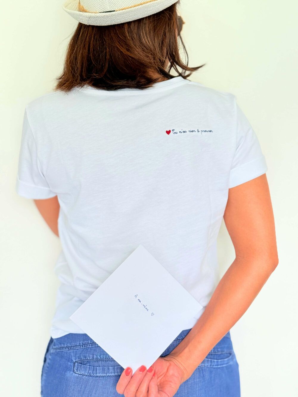 Dos du tee-shirt Soamarena avec message brodé “Tu n’as rien à prouver” et carte manuscrite – look faceless en jean et chapeau