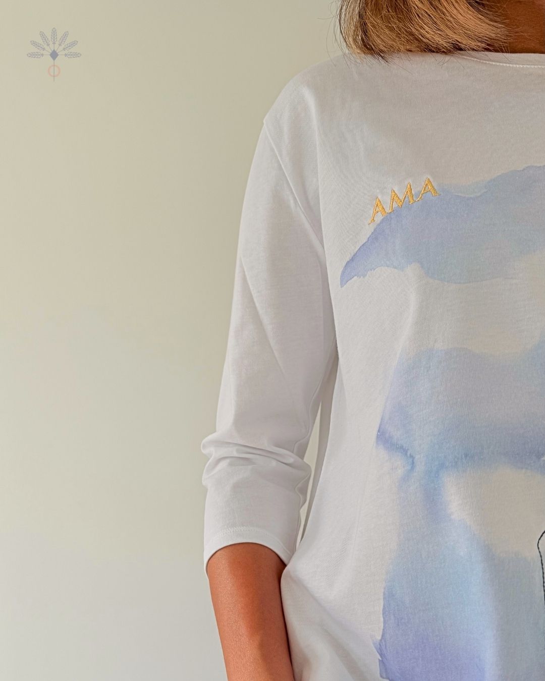 Tee-shirt Soamarena AMA porté par une femme, en coton biologique blanc, avec motif imprimé bleu et texte « AMA » brodé en fil doré.